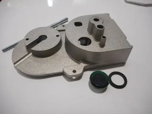 Luftgehäuse von Remeha, aus Metall, mit mehreren Öffnungen und einer abgerundeten Form. Zwei Dichtungen und eine Gewindestange liegen daneben.